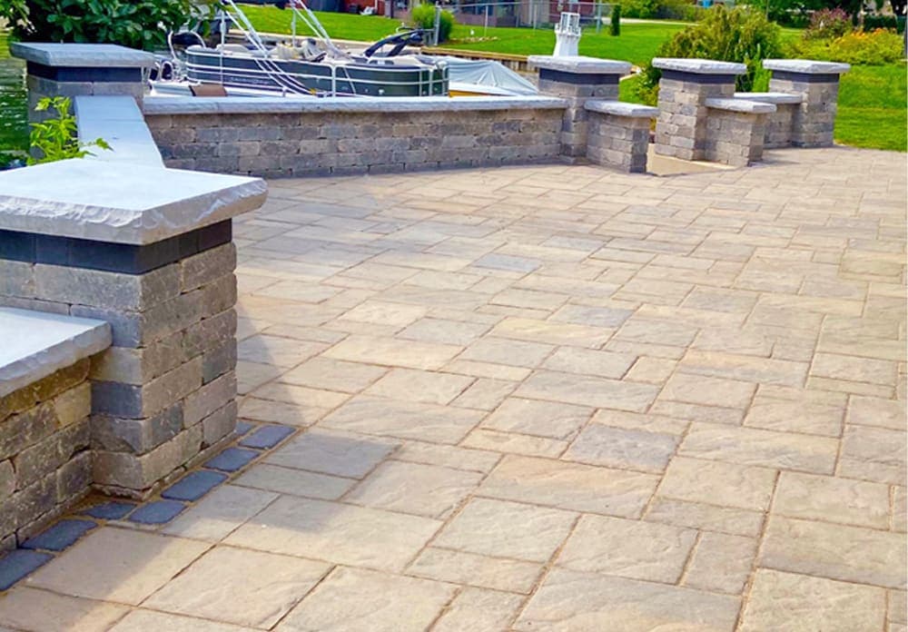 Paved outdoor patio with stone walls and beautiful landscaping in the background.