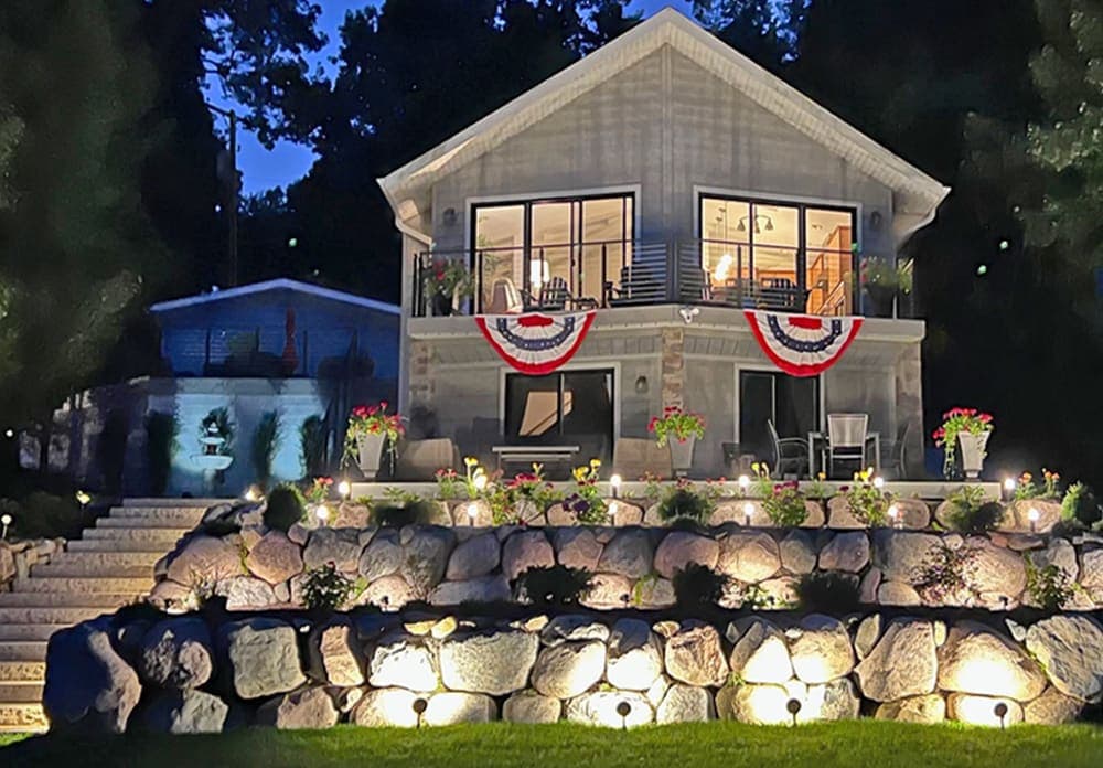 Charming lakefront home at night with festive decorations and illuminated garden features.