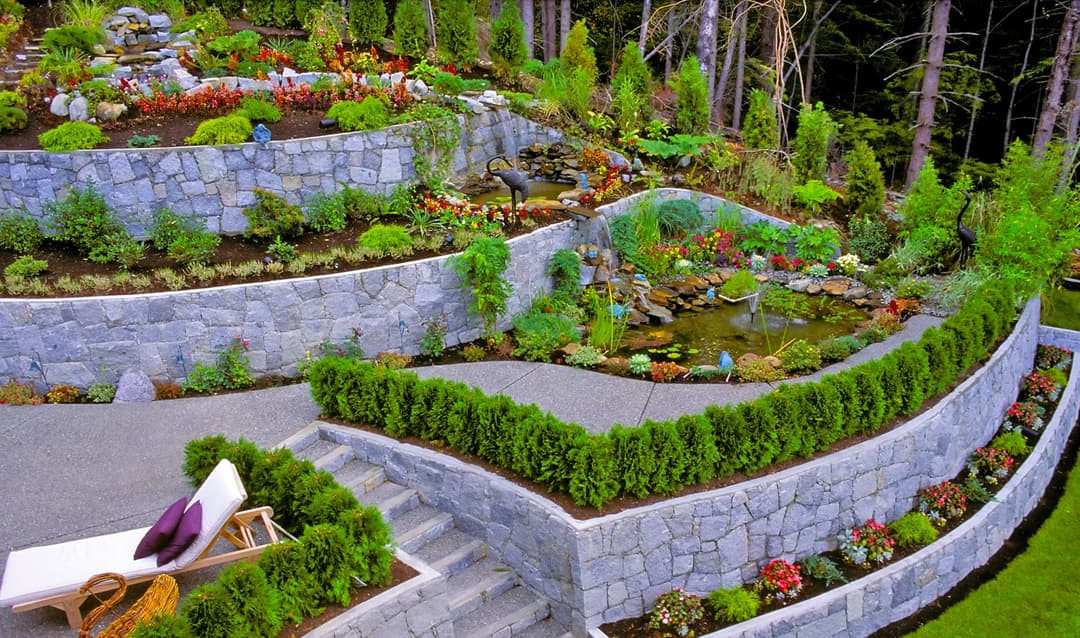 Beautiful landscaped garden with tiered stone walls, colorful flowers, and a small pond.