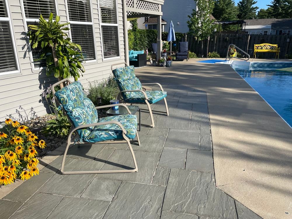 Two colorful lounge chairs by a swimming pool surrounded by flowers and greenery.