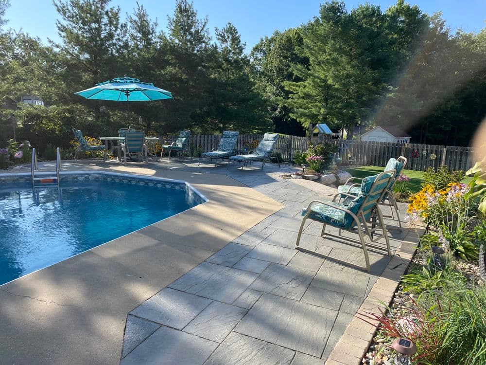 Sunny backyard pool area with lounge chairs, vibrant flowers, and an umbrella.