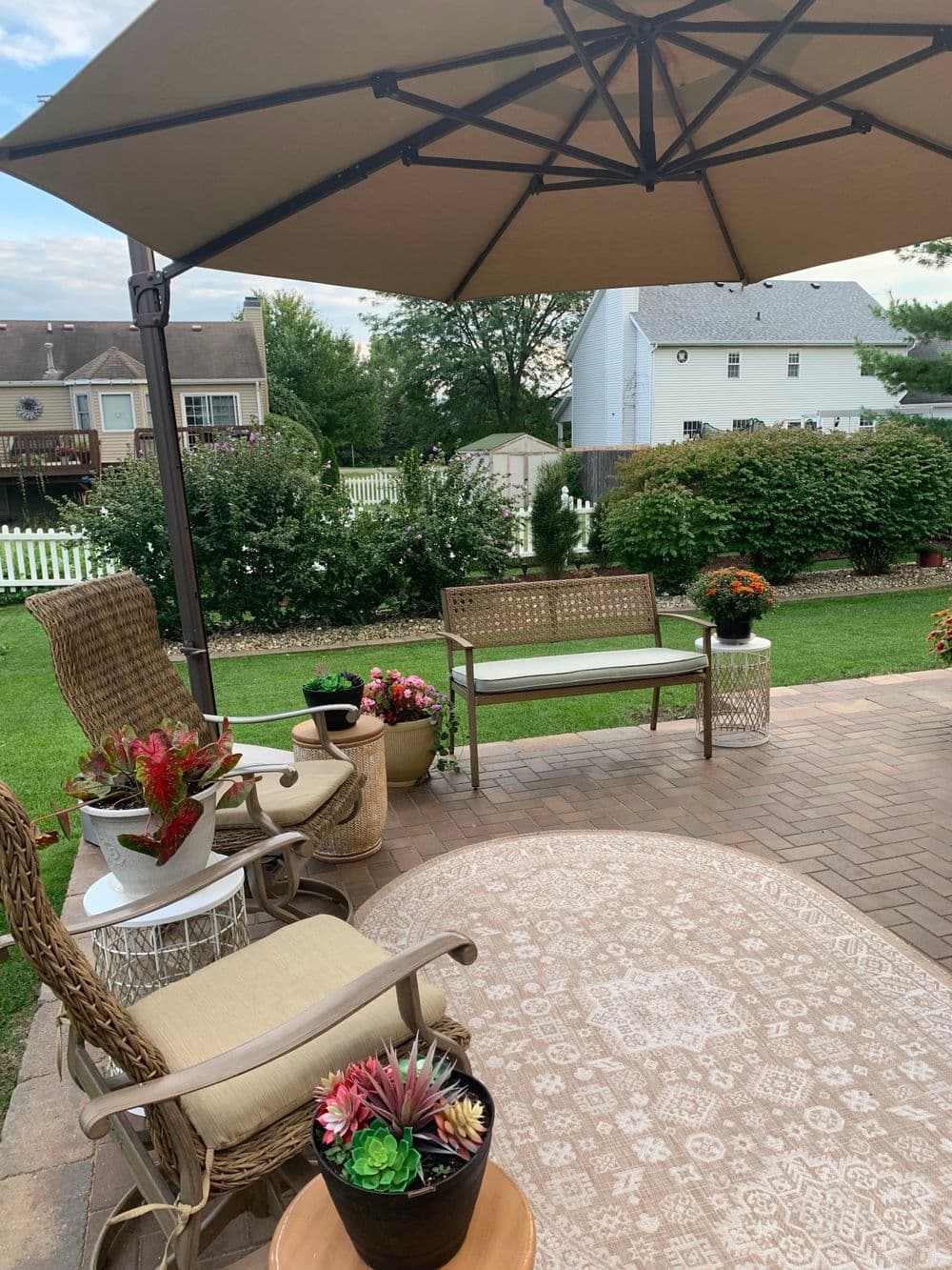 Cozy outdoor patio with chairs, an umbrella, and vibrant plants in a serene garden setting.