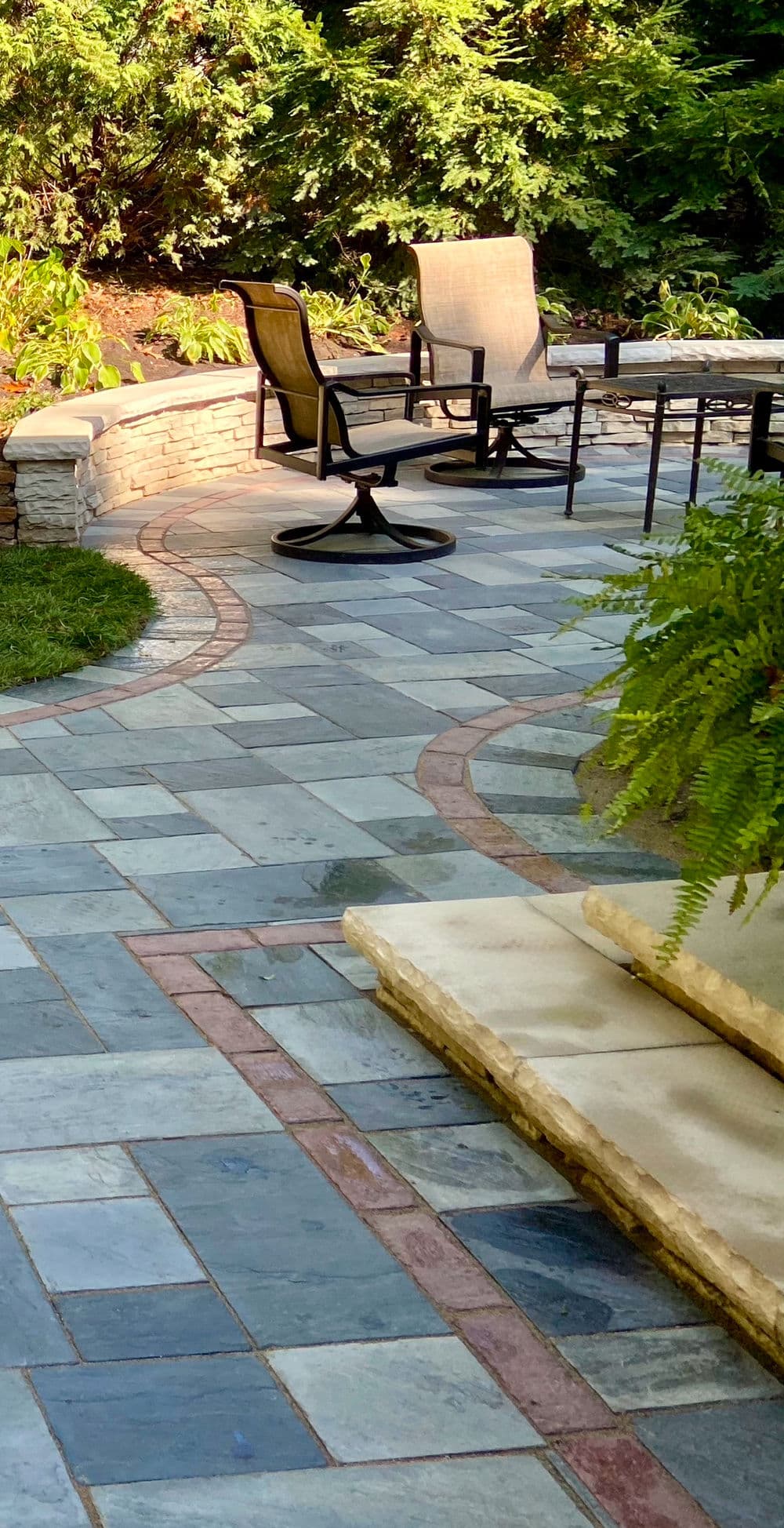 Elegant stone patio with seating area and lush greenery, ideal for outdoor relaxation.
